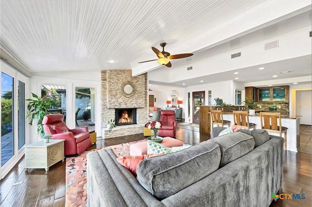 living room featuring dark hardwood / wood-style floors, ceiling fan, a stone fireplace, and lofted ceiling with beams