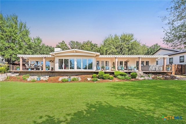 back of house at dusk featuring a pergola, a lawn, and stucco siding