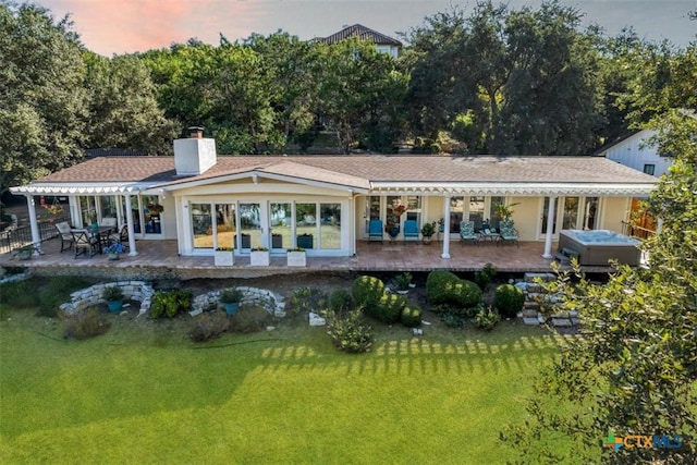 back house at dusk with a hot tub, a lawn, and a patio area