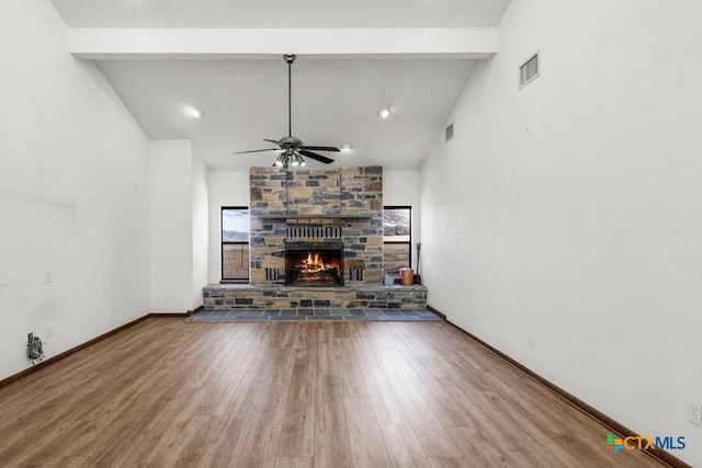 unfurnished living room featuring visible vents, wood finished floors, beamed ceiling, and a stone fireplace