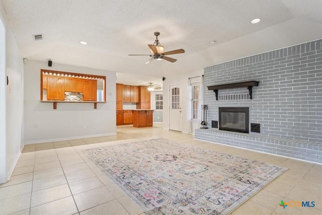 unfurnished living room featuring ceiling fan, brick wall, a textured ceiling, a fireplace, and light tile patterned flooring