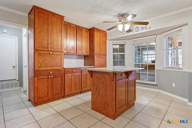 kitchen featuring ceiling fan, light tile patterned floors, light stone counters, crown molding, and a kitchen island