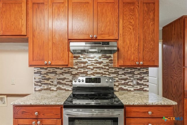 kitchen with light stone counters, stainless steel stove, backsplash, and exhaust hood