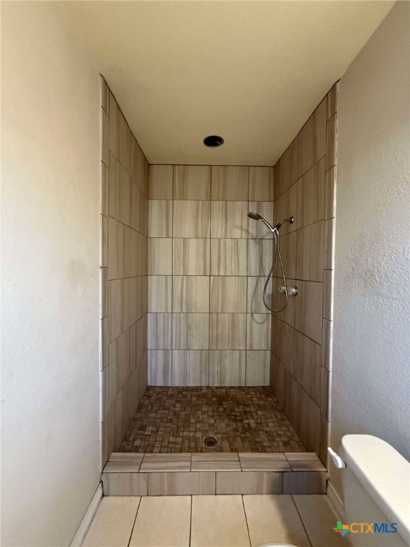 full bath with tile patterned flooring, a tile shower, and toilet