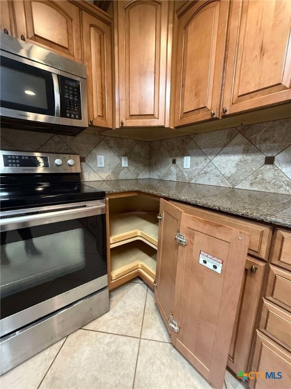 kitchen featuring tasteful backsplash, light tile patterned floors, dark stone counters, and appliances with stainless steel finishes