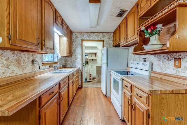kitchen with electric stove, sink, light hardwood / wood-style flooring, a textured ceiling, and butcher block counters