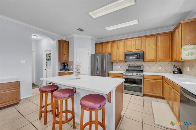 kitchen featuring a kitchen bar, appliances with stainless steel finishes, backsplash, a center island, and light tile patterned flooring