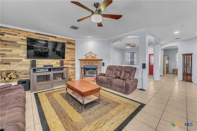 tiled living room featuring ceiling fan, wood walls, crown molding, and a brick fireplace