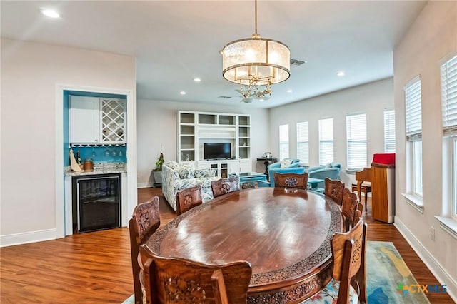 dining room with wood-type flooring, beverage cooler, a chandelier, and bar area