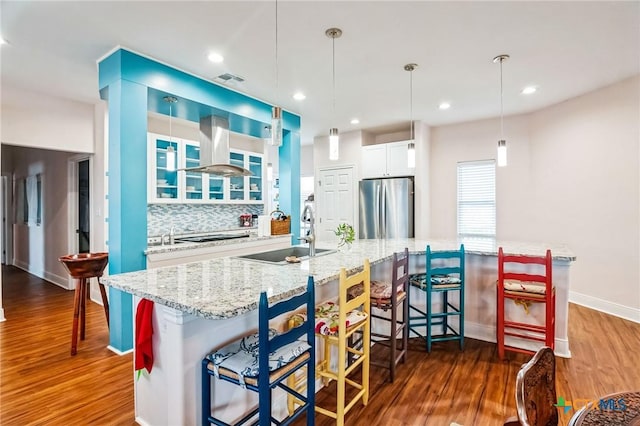 kitchen with sink, stainless steel refrigerator, white cabinetry, extractor fan, and a kitchen bar