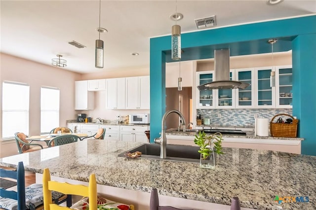 kitchen with white cabinetry, hanging light fixtures, island range hood, and tasteful backsplash