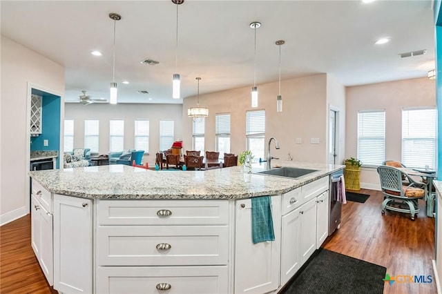 kitchen with sink, hanging light fixtures, white cabinets, and a center island with sink