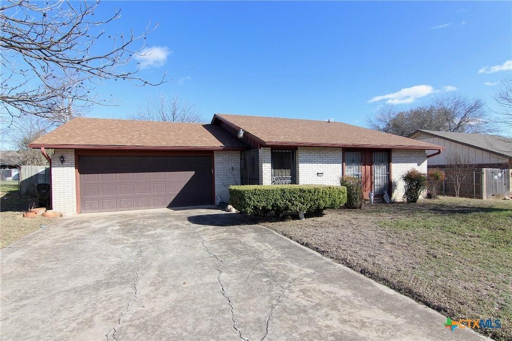 ranch-style house featuring fence, roof with shingles, concrete driveway, an attached garage, and brick siding