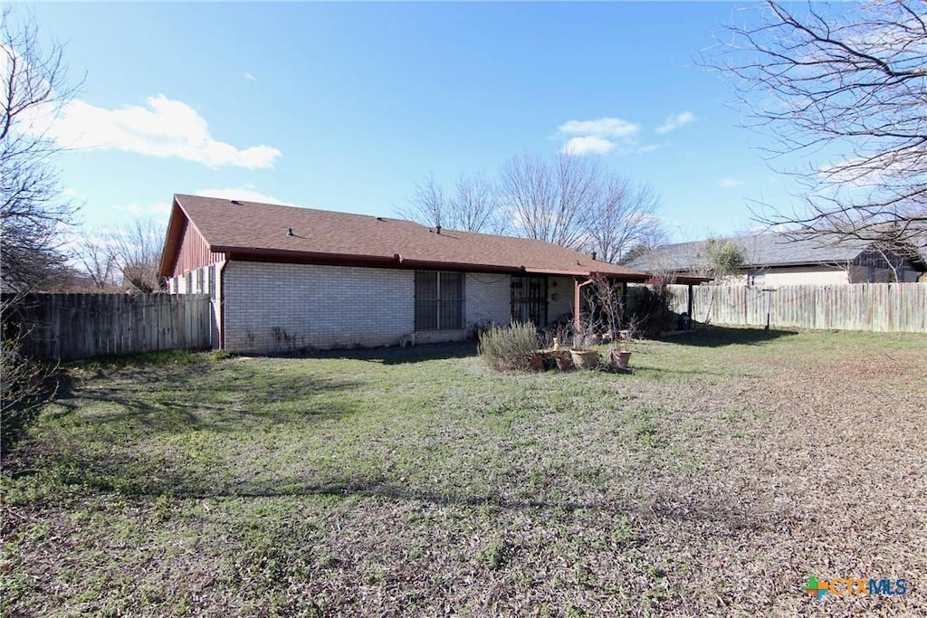 rear view of house with brick siding, a yard, and a fenced backyard