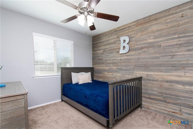 carpeted bedroom featuring an accent wall, baseboards, wood walls, and ceiling fan