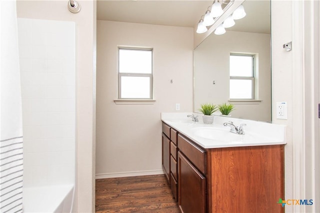 full bath with a sink, shower / washtub combination, wood finished floors, double vanity, and baseboards