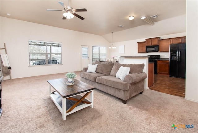 carpeted living room with visible vents, ceiling fan with notable chandelier, and vaulted ceiling