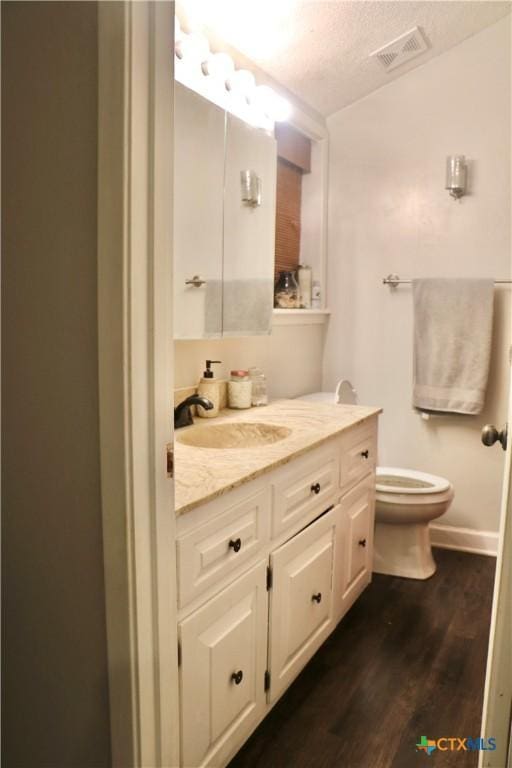 bathroom featuring a textured ceiling, toilet, wood finished floors, vanity, and visible vents