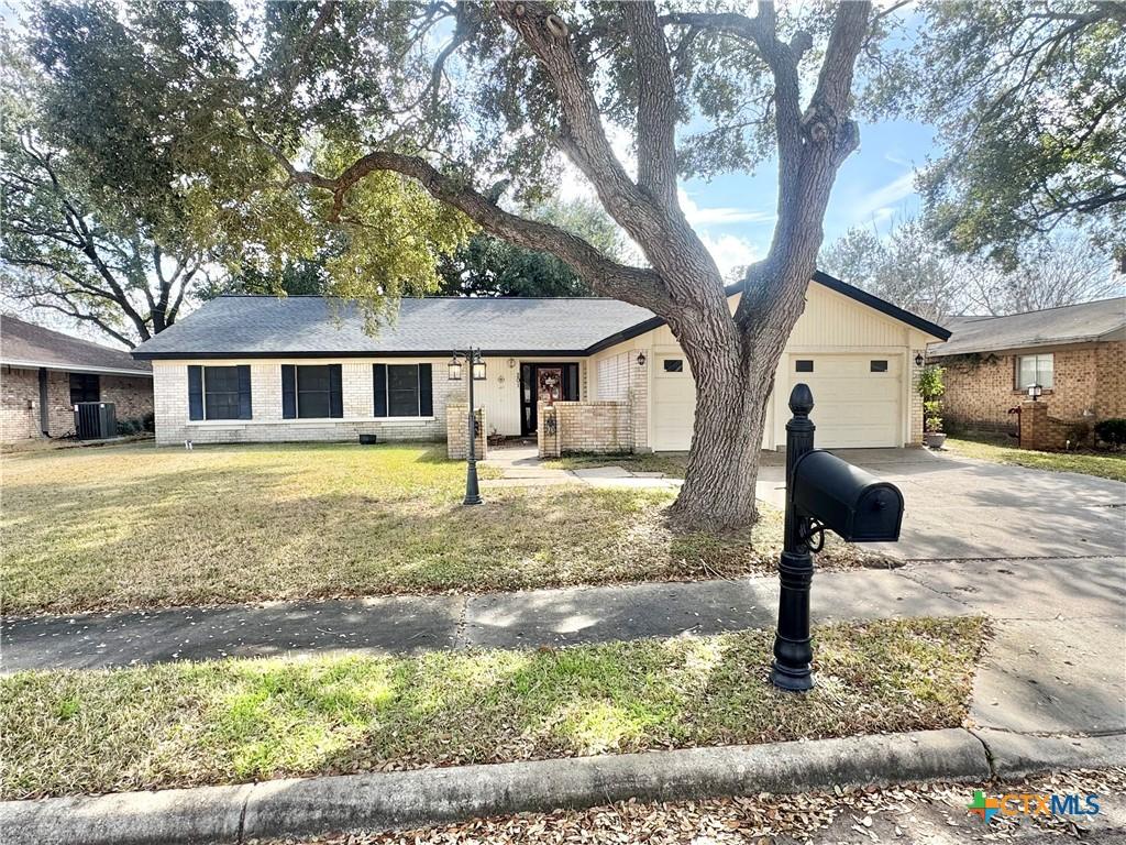 ranch-style home with an attached garage, central air condition unit, brick siding, concrete driveway, and a front lawn