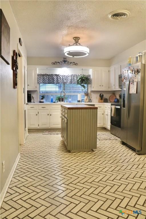 kitchen with visible vents, a kitchen island, appliances with stainless steel finishes, light countertops, and white cabinetry