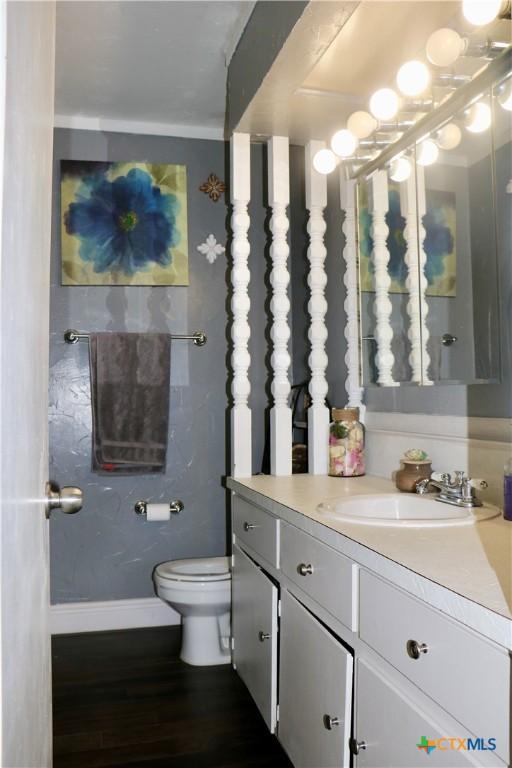 bathroom with toilet, wood finished floors, vanity, and baseboards