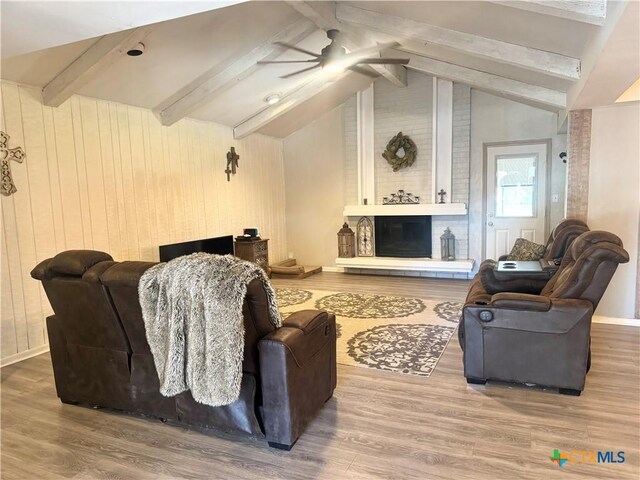 living room featuring vaulted ceiling with beams, ceiling fan, a fireplace, and wooden walls