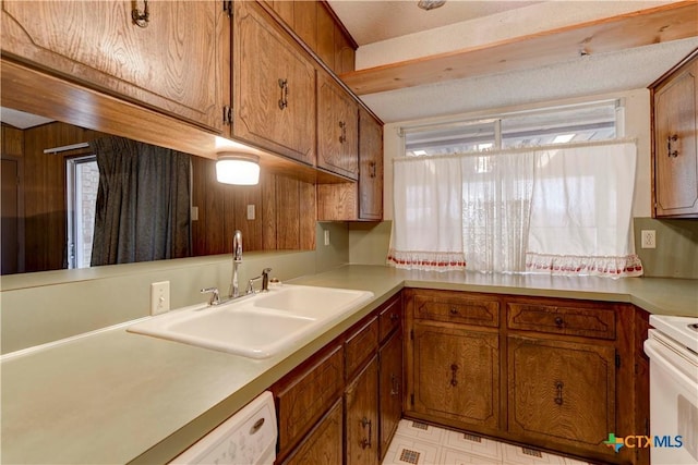 kitchen with white appliances, a sink, light countertops, light floors, and brown cabinetry