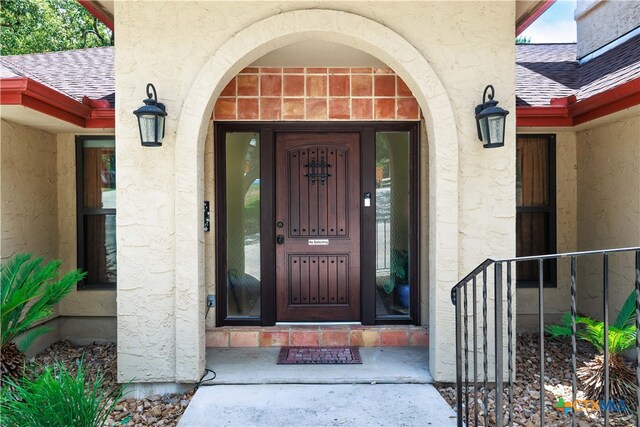 view of exterior entry with a shingled roof and stucco siding