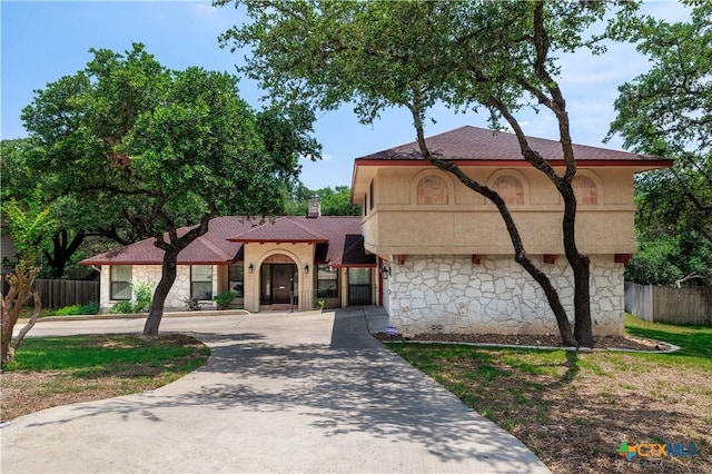 mediterranean / spanish house featuring a chimney, fence, curved driveway, and a shingled roof