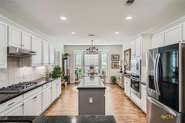 kitchen with white cabinets, appliances with stainless steel finishes, a center island, tasteful backsplash, and hanging light fixtures