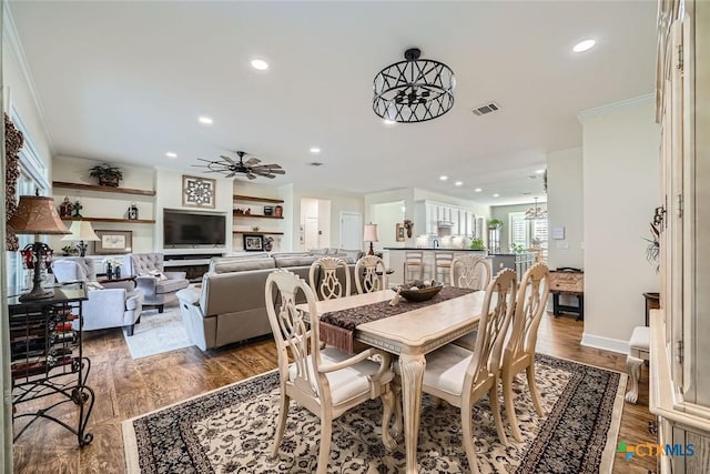 dining room with ceiling fan with notable chandelier, hardwood / wood-style floors, built in features, and crown molding