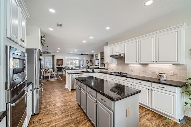 kitchen featuring kitchen peninsula, white cabinets, dark stone countertops, a kitchen island, and stainless steel appliances