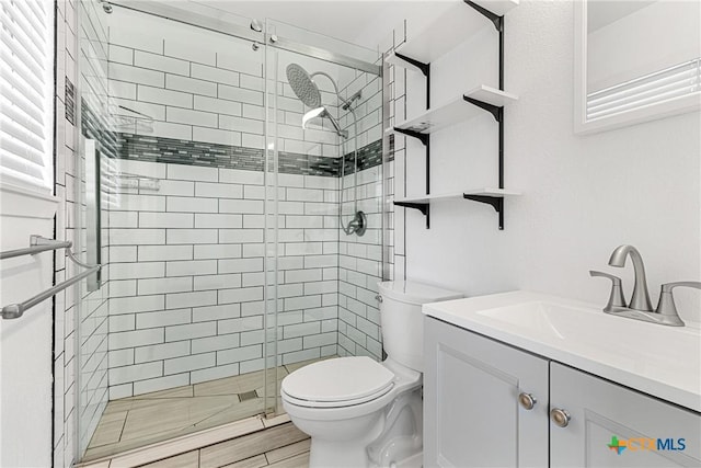 bathroom featuring a shower with door, toilet, and vanity