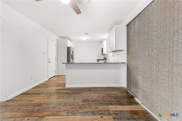 kitchen with light stone countertops, appliances with stainless steel finishes, white cabinetry, decorative backsplash, and kitchen peninsula