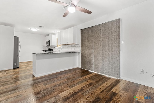 kitchen featuring white cabinetry, stainless steel appliances, dark stone counters, tasteful backsplash, and kitchen peninsula