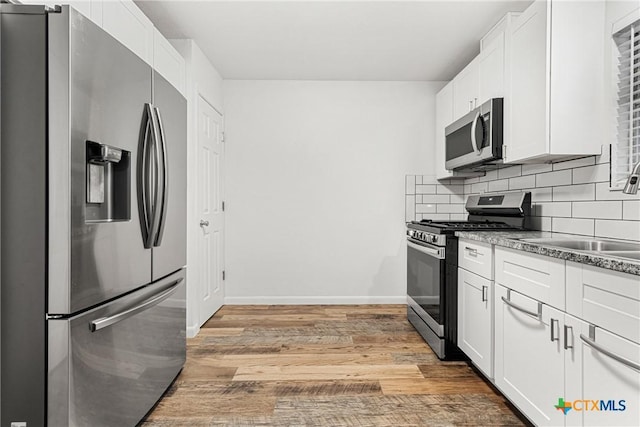 kitchen featuring white cabinets, appliances with stainless steel finishes, decorative backsplash, sink, and light wood-type flooring