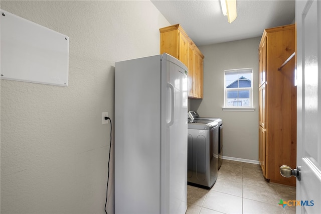 clothes washing area featuring separate washer and dryer, light tile patterned floors, cabinets, and a textured ceiling