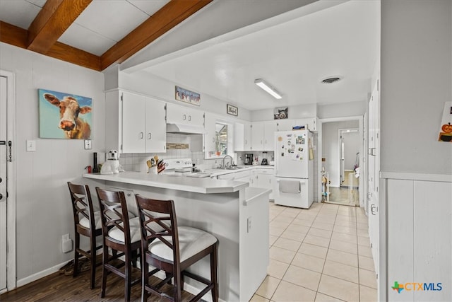 kitchen featuring white cabinetry, white appliances, beam ceiling, a kitchen breakfast bar, and kitchen peninsula