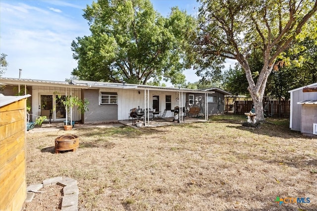 rear view of property with a fire pit, a lawn, a storage unit, and a patio area