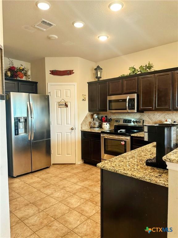 kitchen with light stone counters, tasteful backsplash, dark brown cabinetry, stainless steel appliances, and visible vents