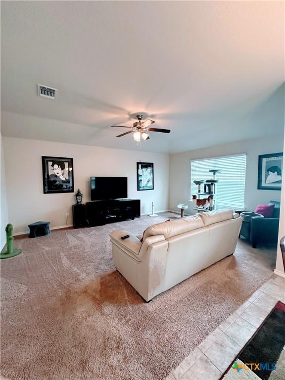 carpeted living room with visible vents, a ceiling fan, baseboards, and tile patterned floors