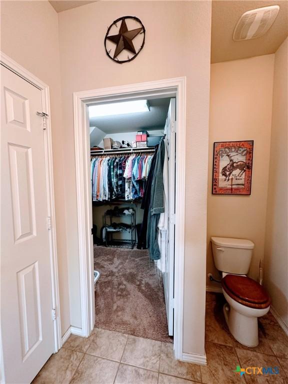 bathroom with tile patterned floors, visible vents, toilet, a walk in closet, and baseboards