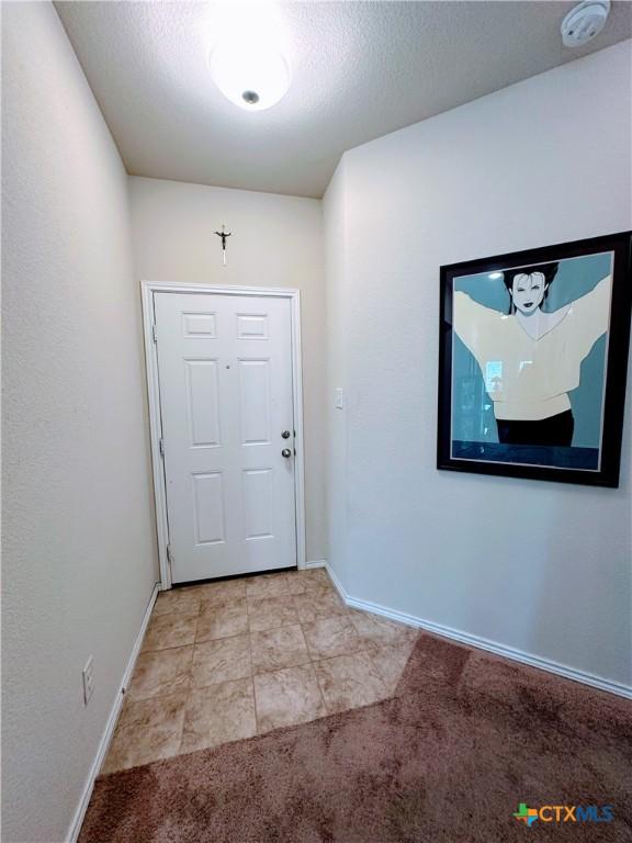 doorway with a textured ceiling, baseboards, and light carpet