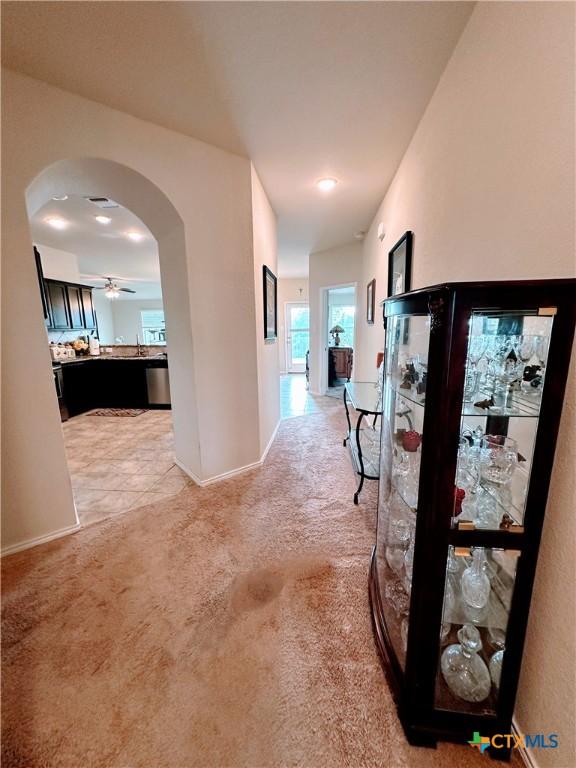 hall with baseboards, arched walkways, and light colored carpet