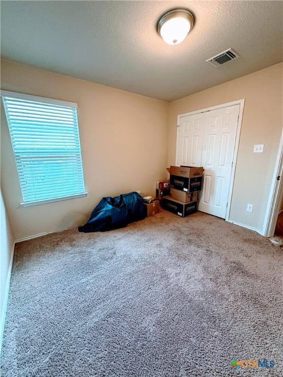 unfurnished bedroom with a textured ceiling, baseboards, visible vents, a closet, and carpet floors