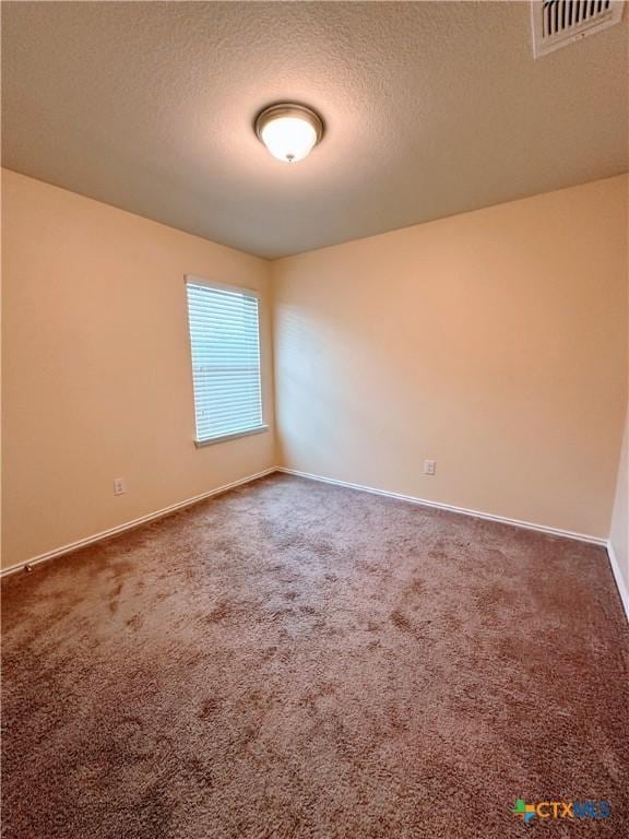 empty room with carpet floors, a textured ceiling, visible vents, and baseboards