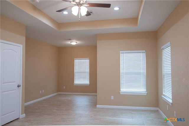 spare room with ceiling fan, light hardwood / wood-style floors, a raised ceiling, and a wealth of natural light