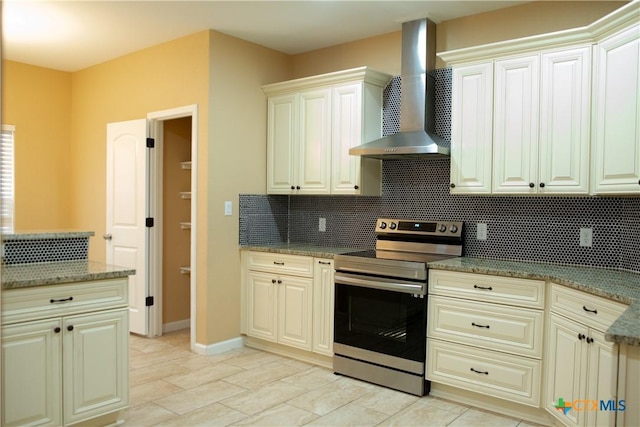 kitchen with wall chimney range hood, tasteful backsplash, cream cabinets, dark stone counters, and stainless steel electric stove