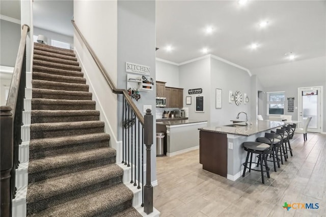 kitchen featuring an island with sink, sink, a kitchen bar, ornamental molding, and light wood-type flooring