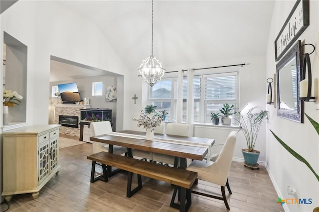 dining space featuring an inviting chandelier, high vaulted ceiling, a stone fireplace, and light hardwood / wood-style floors